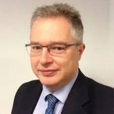 Steven Segal, head and shoulders, in glasses, a dark suit and a blue tie against an office wall.